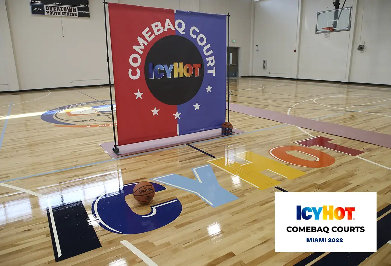 An image of the newly renovated basketball court at Overtown Youth Center (OYC) in Miami, Florida, showcasing the vibrant Icy Hot logo prominently on the floor. In the lower-right corner of the image, a label displays the Icy Hot Comebaq Courts logo, along with the event's year (2022) and location (Miami).