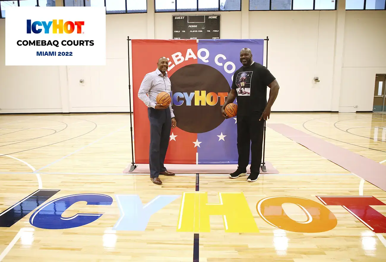 Shaquille O'Neal and Alonzo Mourning posing proudly in front of the Comebaq Court sign on the newly renovated basketball court at Overtown Youth Center (OYC) in Miami, Florida. The court features the distinctive Icy Hot logo. In the upper-left corner of the image, a label displays the Icy Hot Comebaq Courts logo, along with the event's year (2022) and location (Miami).