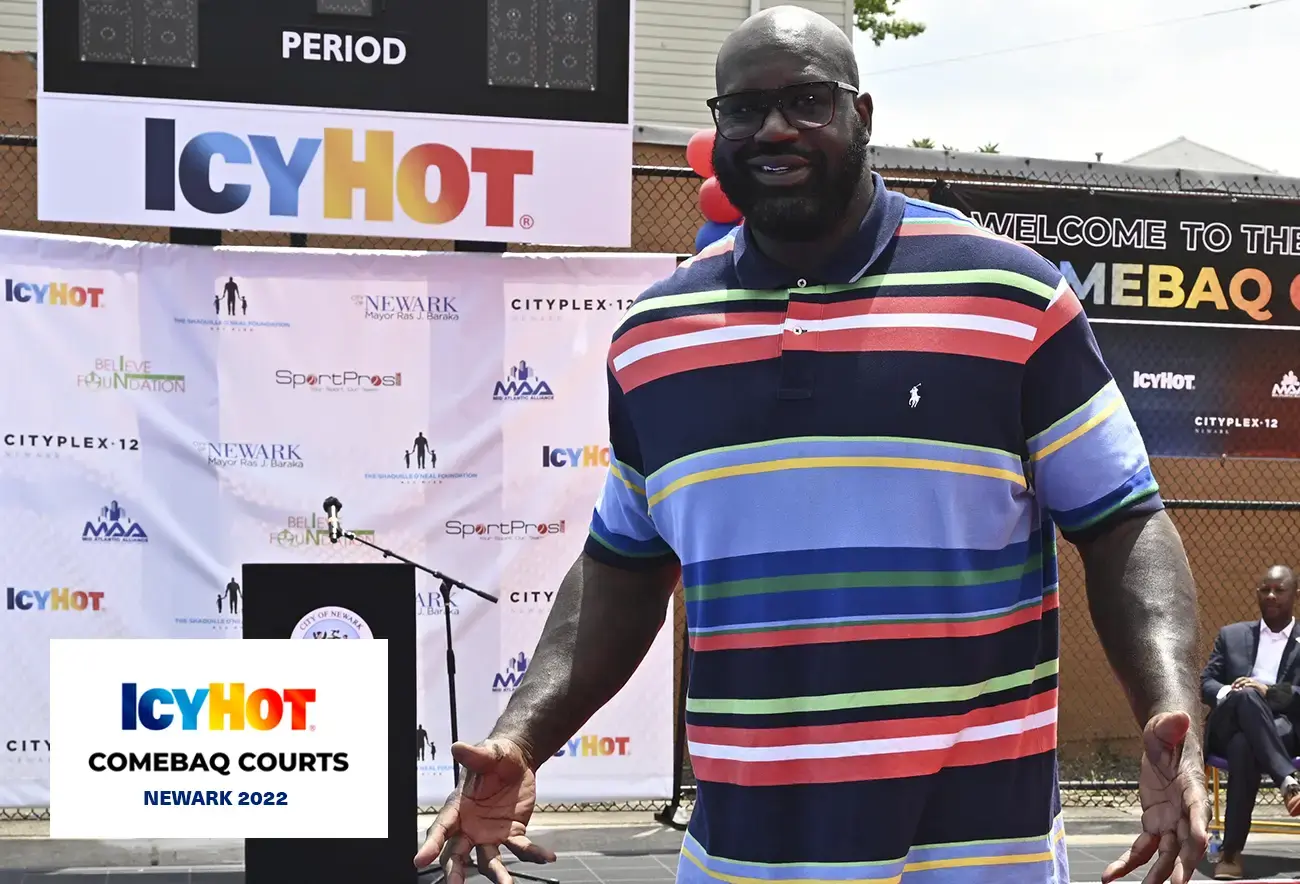 Shaquille O'Neal standing in front of the podium during the press event, unveiling the newly renovated basketball court in Newark. The lower-left corner of the image features a label displaying the Icy Hot Comebaq Courts logo, along with the event's year (2022) and location (Newark).