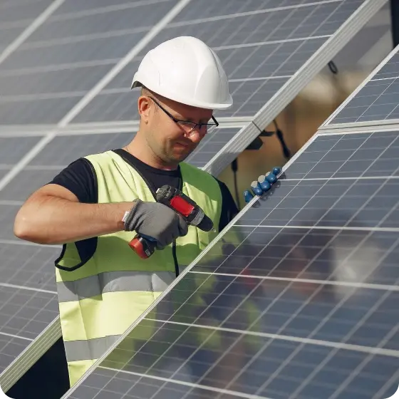 Un homme portant un casque de sécurité et un gilet de sécurité travaillant avec diligence sur des panneaux solaires.