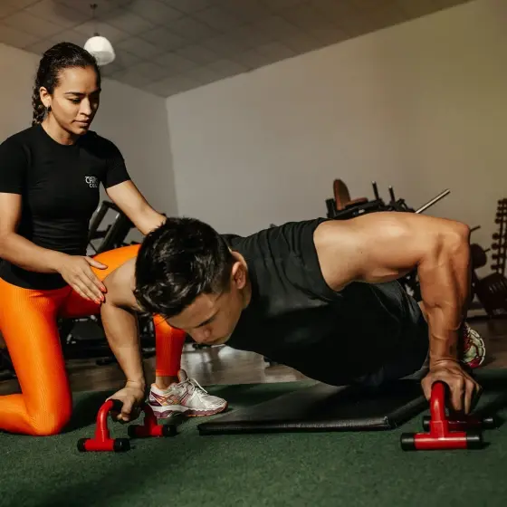 A male athlete doing pushups, while a female athlete kneels at his side, assisting him.