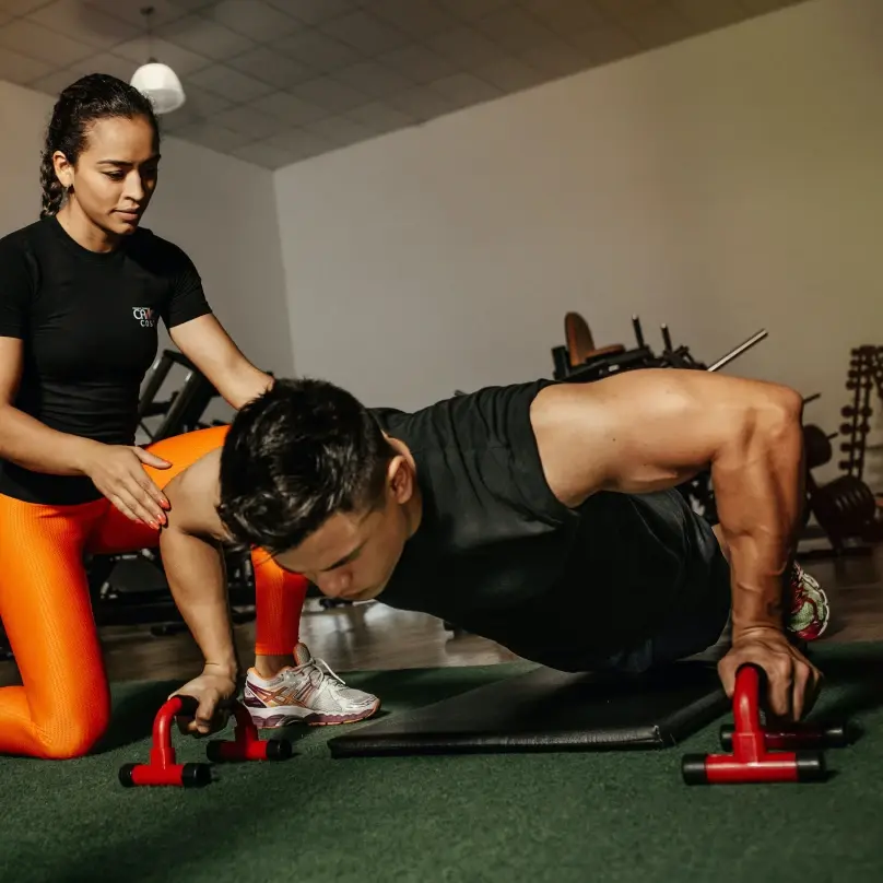 A male athlete doing pushups, while a female athlete kneels at his side, assisting him.